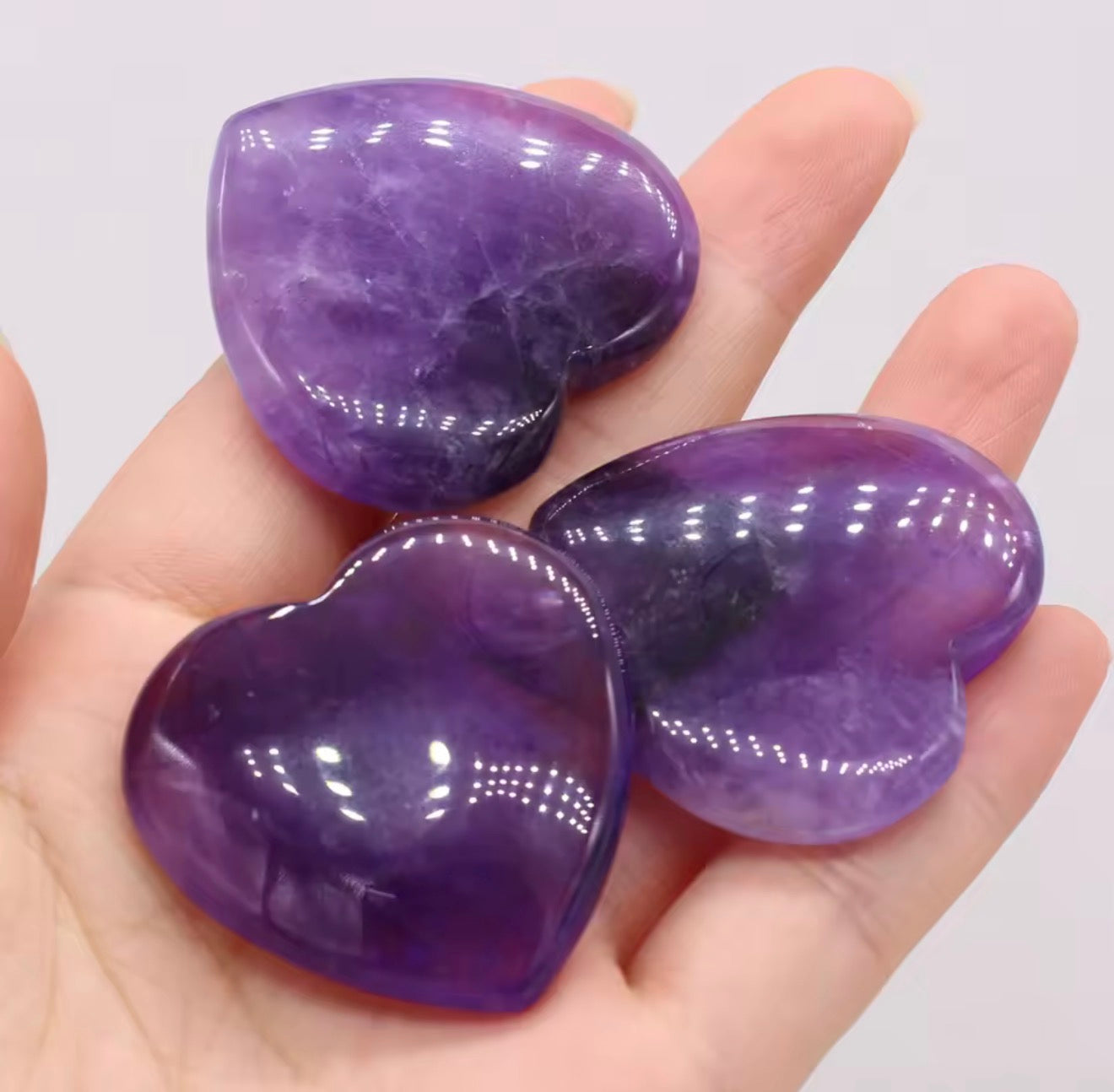 Natural amethyst crystal hearts held in hand showing deep violet colour