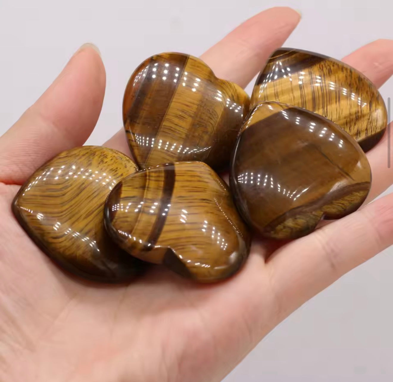 Natural tiger eye crystal hearts held in hand showing golden brown chatoyant bands