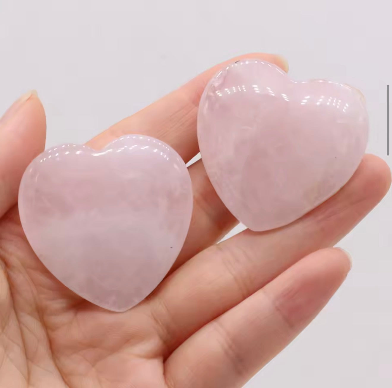Natural rose quartz crystal hearts held in hand showing soft blush pink colour