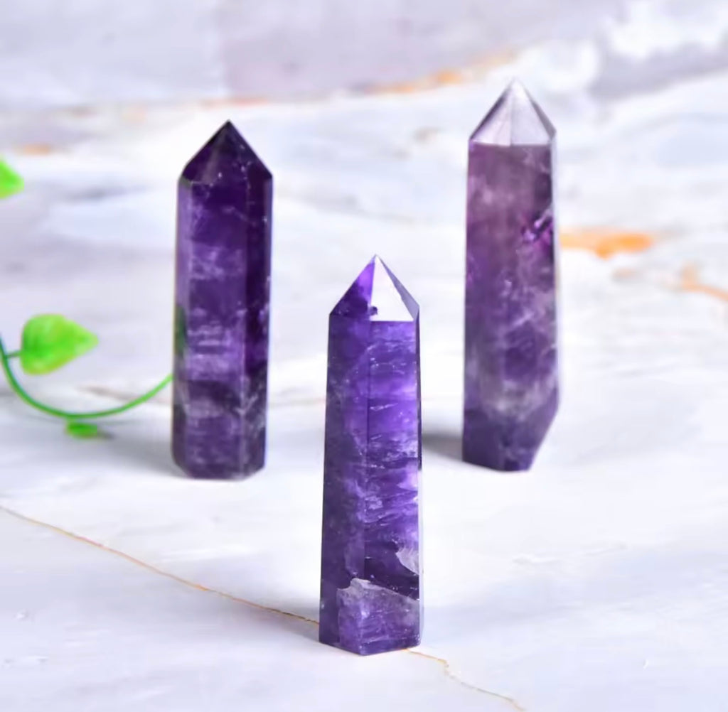 Natural amethyst crystal point towers in three sizes on marble surface