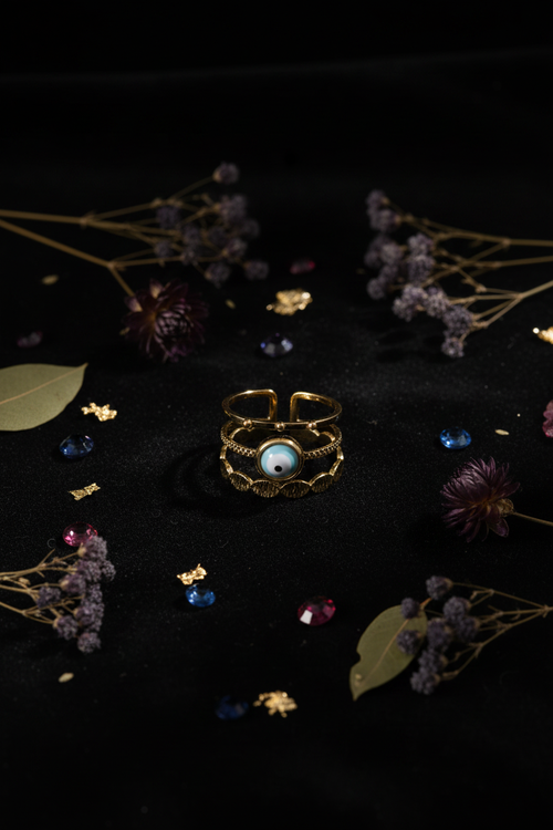Evil Eye 3-Layer Ring portrait flat lay on dark velvet with dried flowers and gemstone crystals — moody editorial luxury jewelry photography
